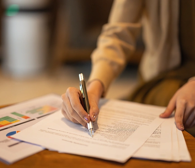 Person filling out paperwork with a pen, surrounded by documents and charts, representing the preparation for a psychiatric evaluation at A Helping Hand Counseling.
