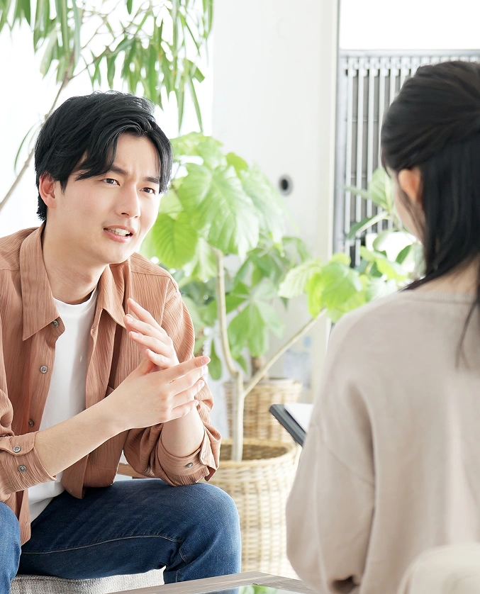 Man engaged in a conversation with a psychiatrist during a mental health evaluation session, discussing symptoms and personal background in a calming, plant-filled environment.